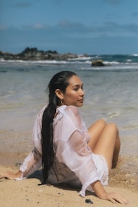 a woman sitting on the beach with long hair