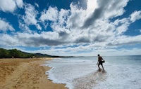 a man is walking on a beach in front of a cloudy sky